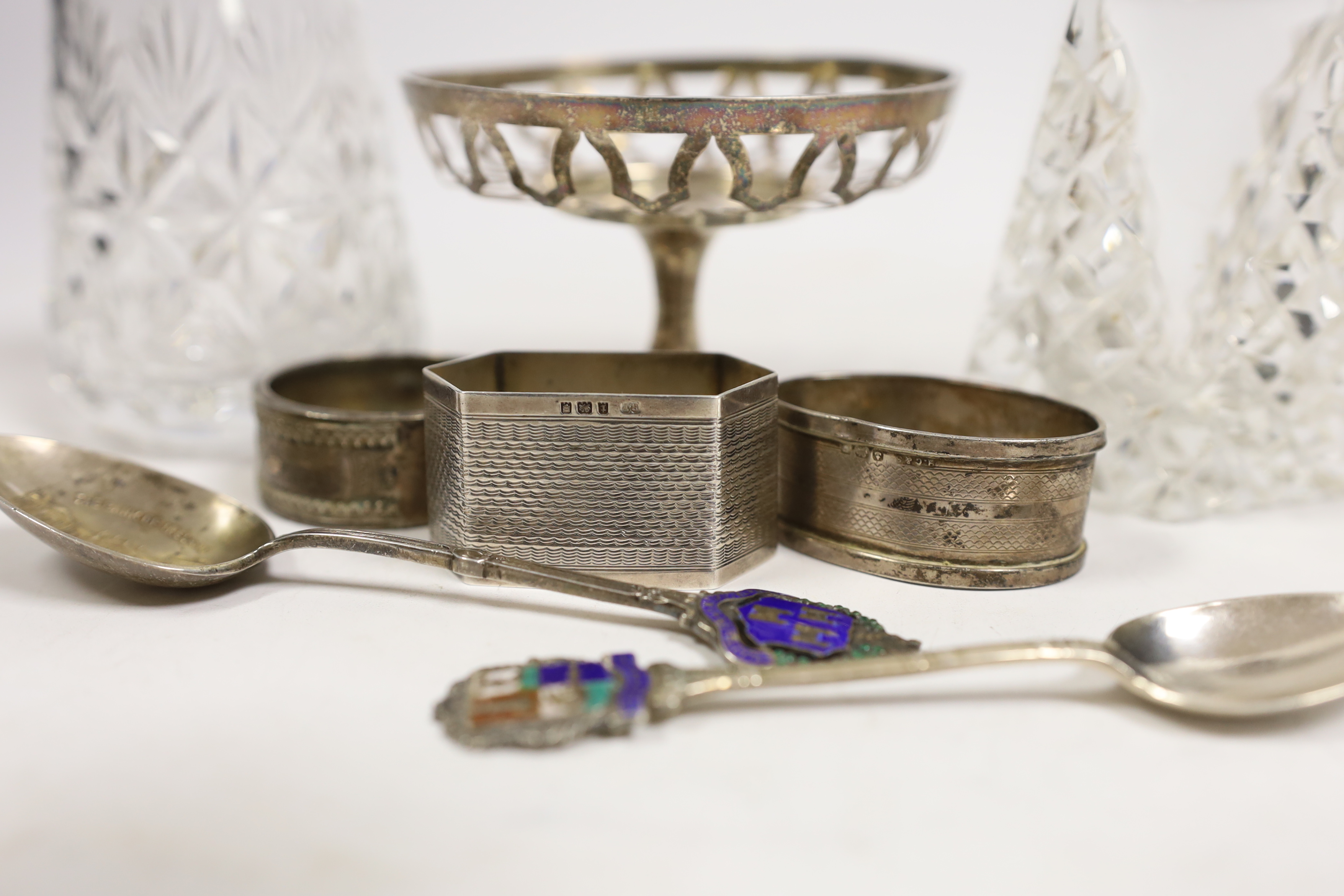 A group of small silver including two mounted glass sugar sifters, three assorted napkin rings, two commemorative spoons and a small pedestal nut dish (lacking insert).